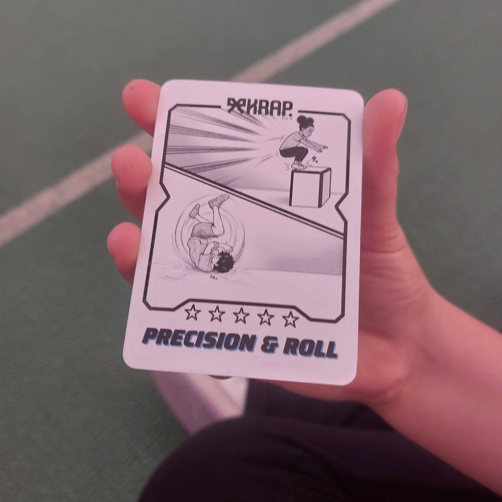 Una mano tiene la skill card KRAP «Precision & Roll», con il disegno del salto e della capriola