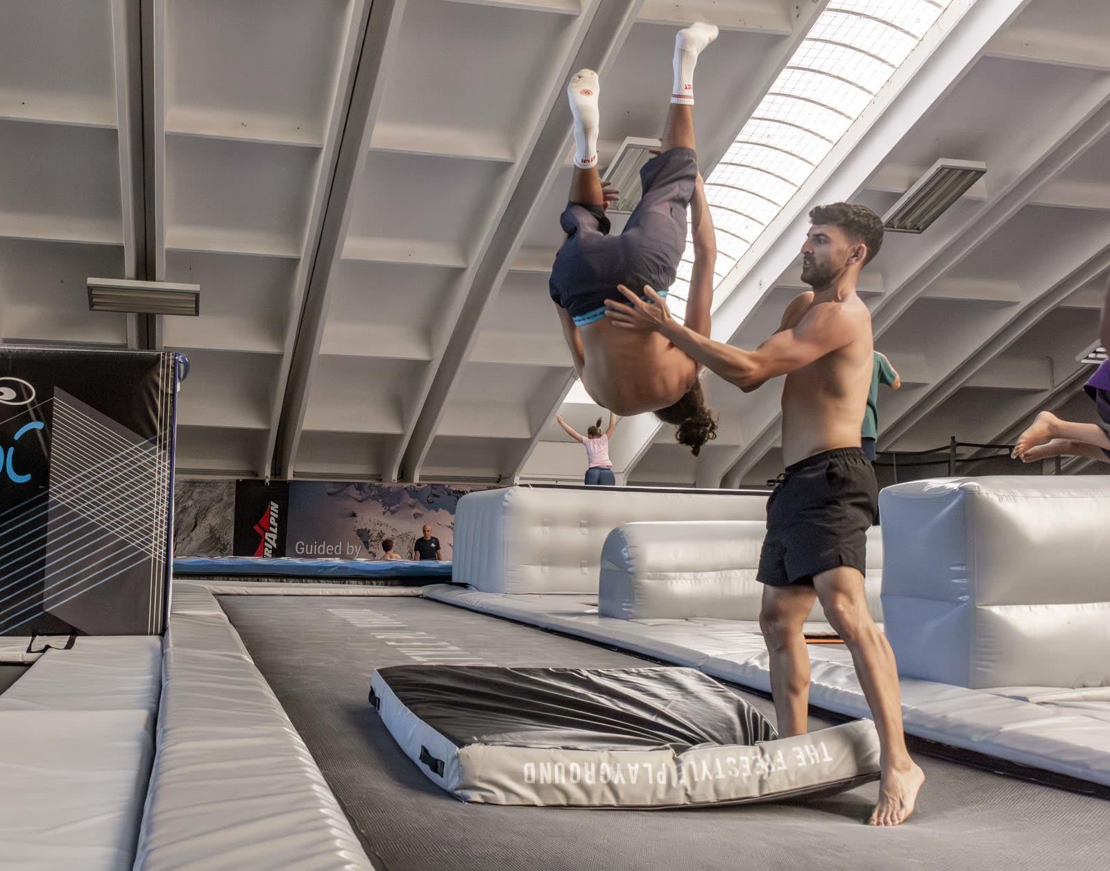 Un coach tiene le mani sulla schiena di un compagno a testa in giù, a metà di un salto all'indietro sul trampolino