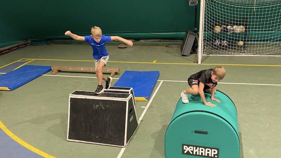 Nella stessa lezione, un bambino cammina sul box alto e un altro supera il rullo basso